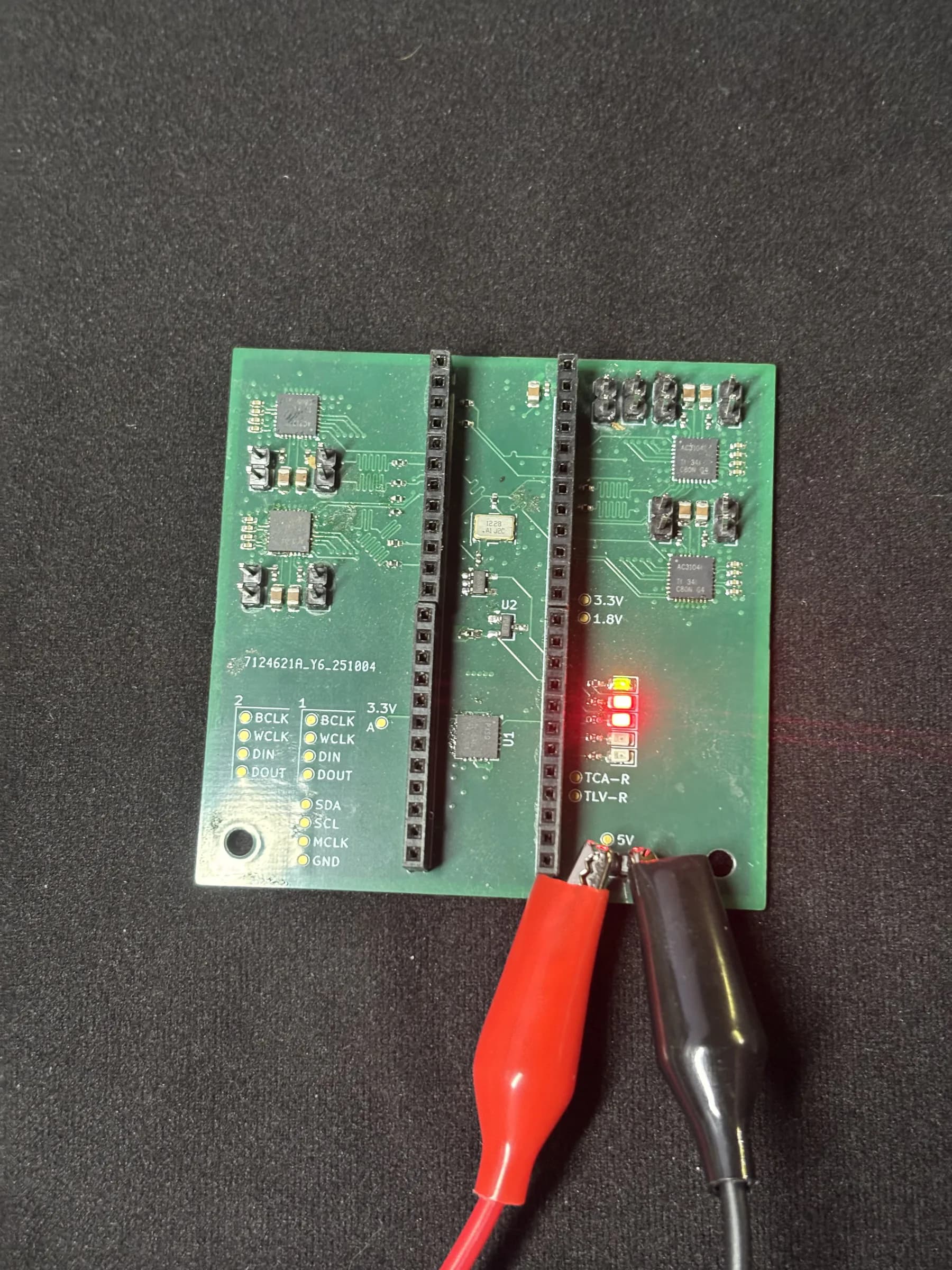 Populated DSP Revision 1 PCB on a work surface with test leads attached.